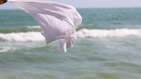 white cloth billows against a backdrop of ocean waves.