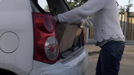 Woman-putting-cardboard-box-into-boot-of-car-wide-shot