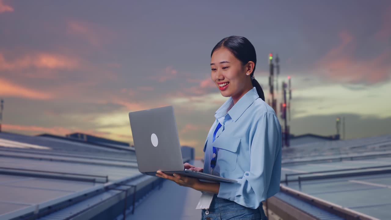 Side View Of Asian Female With Her Laptop, Inspecting Industrial Rooftop Solar Panels, Typing On Her Laptop'S Keybaord With Meditation