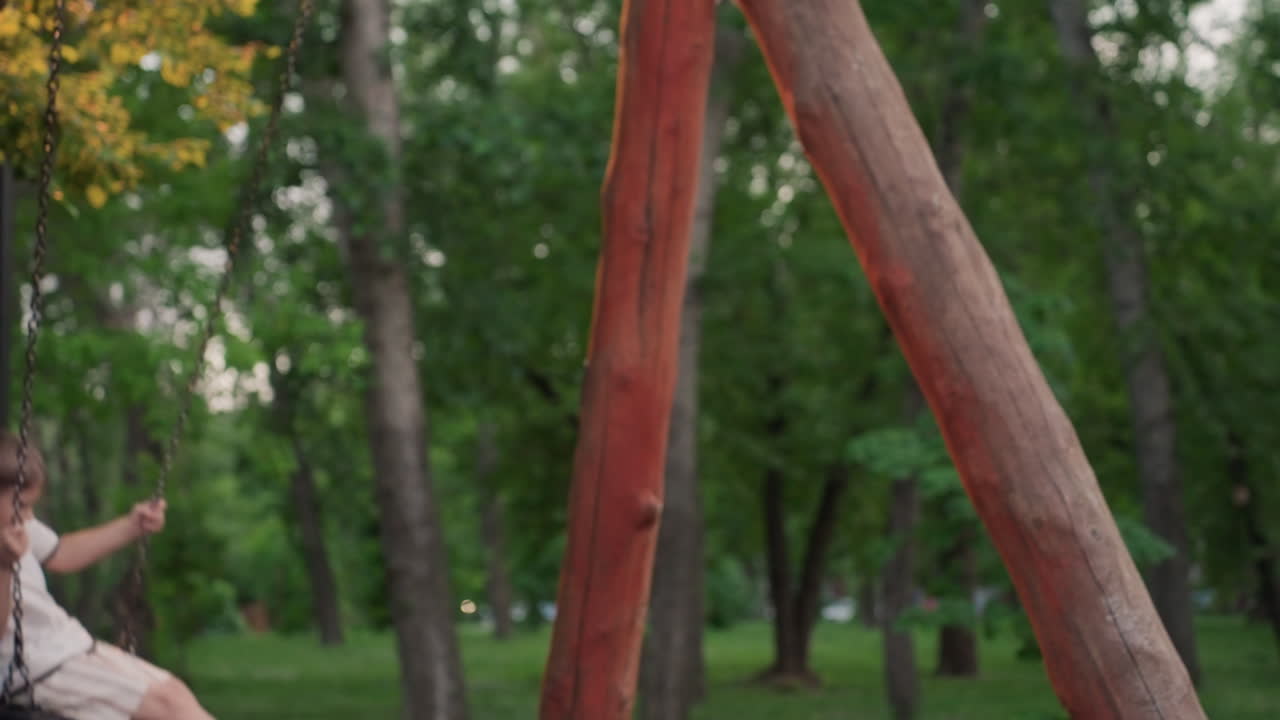 playful boy swinging high on chain swing in leafy park at dusk under warm light capturing carefree moment joyful energy and summer fun outdoors with blurred green background and subtle motion