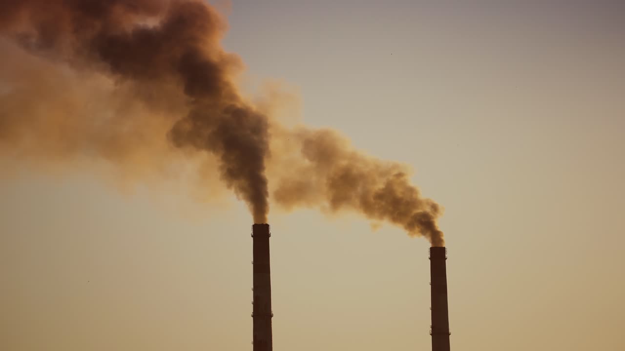 Air pollution by smoke coming out of two factory chimneys. Aerial view.