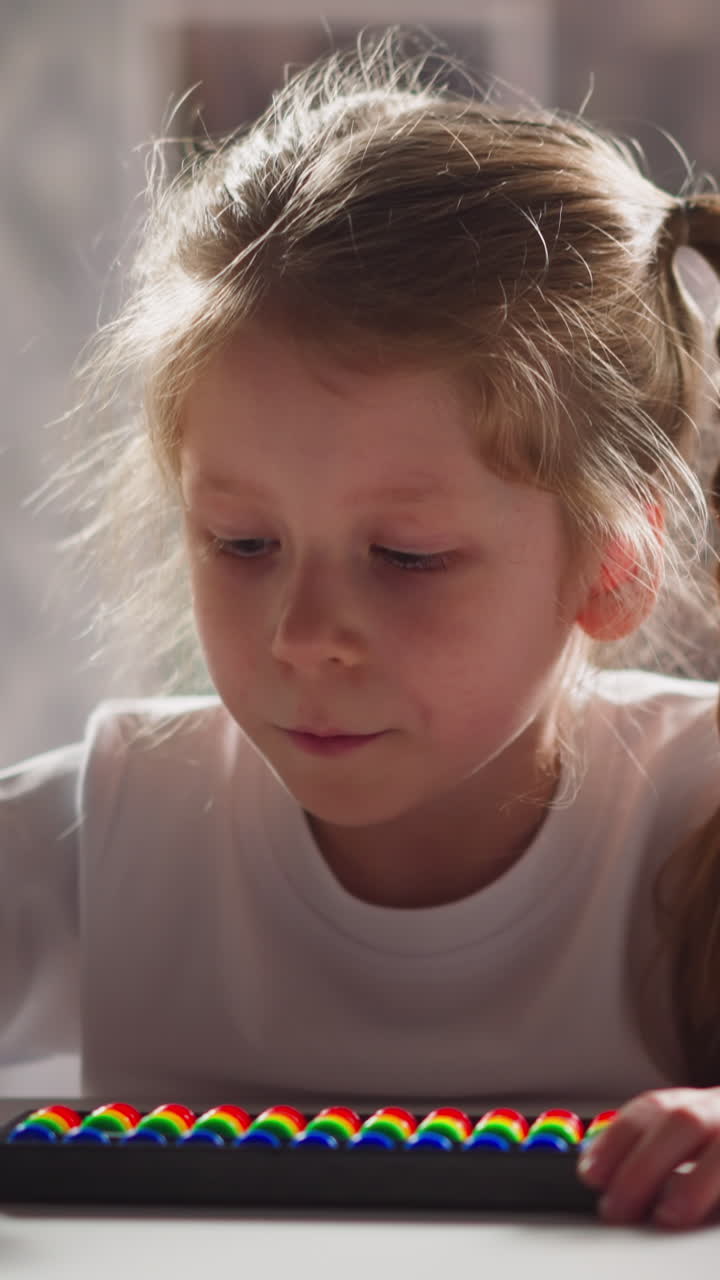 Adorable little child with long plaits counts on colorful abacus doing sums during mental mathematics lesson close view slow motion