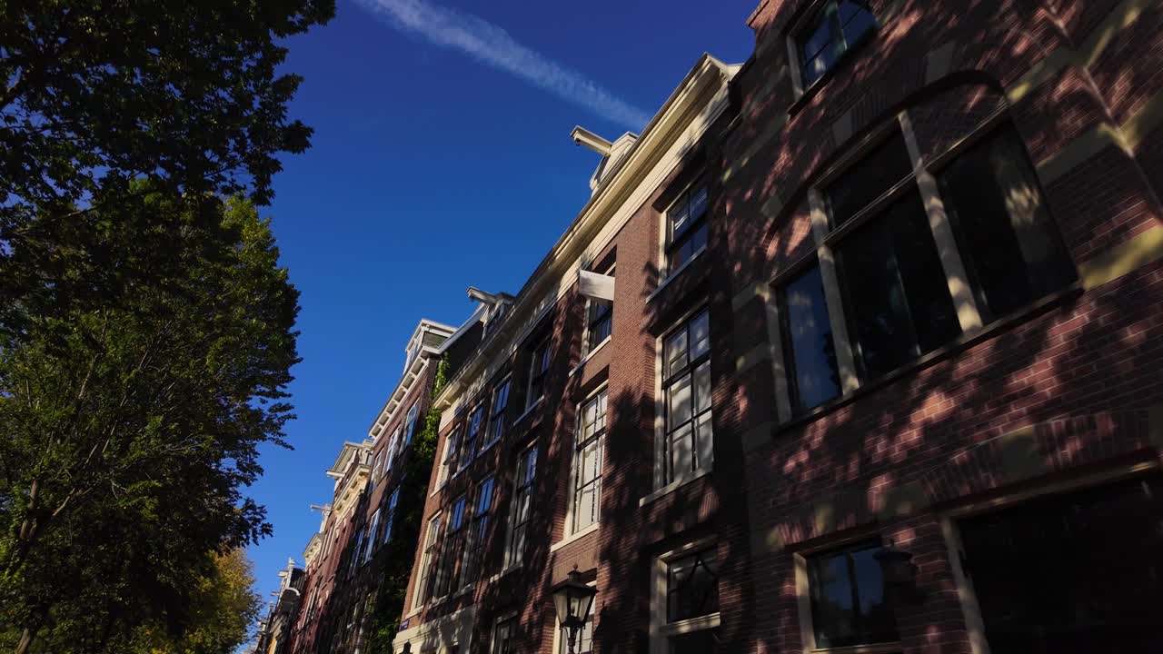 Red brick tower of a historic Amsterdam building surrounded by trees under clear blue sky. Location: Amsterdam, Noord-Holland, Netherlands (Amsterdam, Noord-Holland, Nederland)