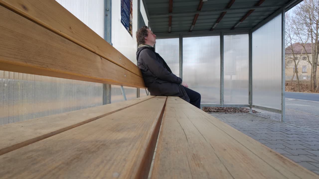 En mand med rygsæk ankommer til busstoppestedet. Han tjekker klokken og venter alene på bussen, der allerede er kørt