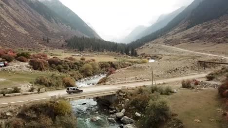 Car-driving-over-the-bridge-looking-down-the-valley-l-view-with-a-beautiful-mountain-river-running-underneath