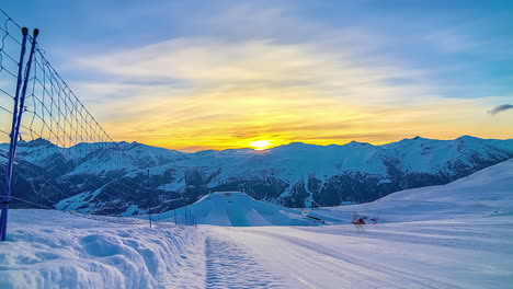 snowy landscape with a wire fence and a mountainous horizon under a golden sky at sunset