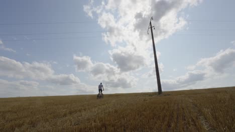 man rides mountain bike through open grassy farm fields below concrete utility pole, blue sky