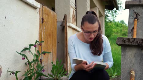 una joven leyendo cerca de una casa antigua en la naturaleza