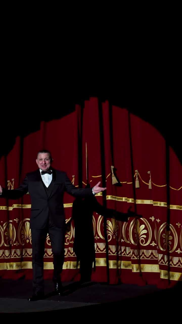 Actor appears on stage. Red curtains open and a theater host in suit comes on the scene on dark background in light spot. Vertical video