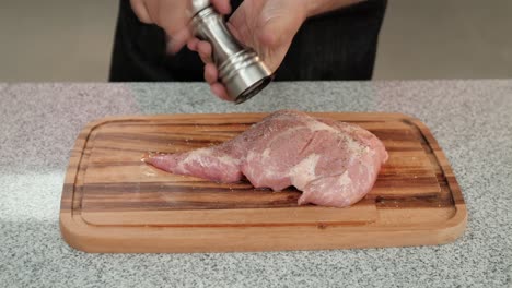 primer plano de un chef agregando pimienta a una carne de cerdo cruda
