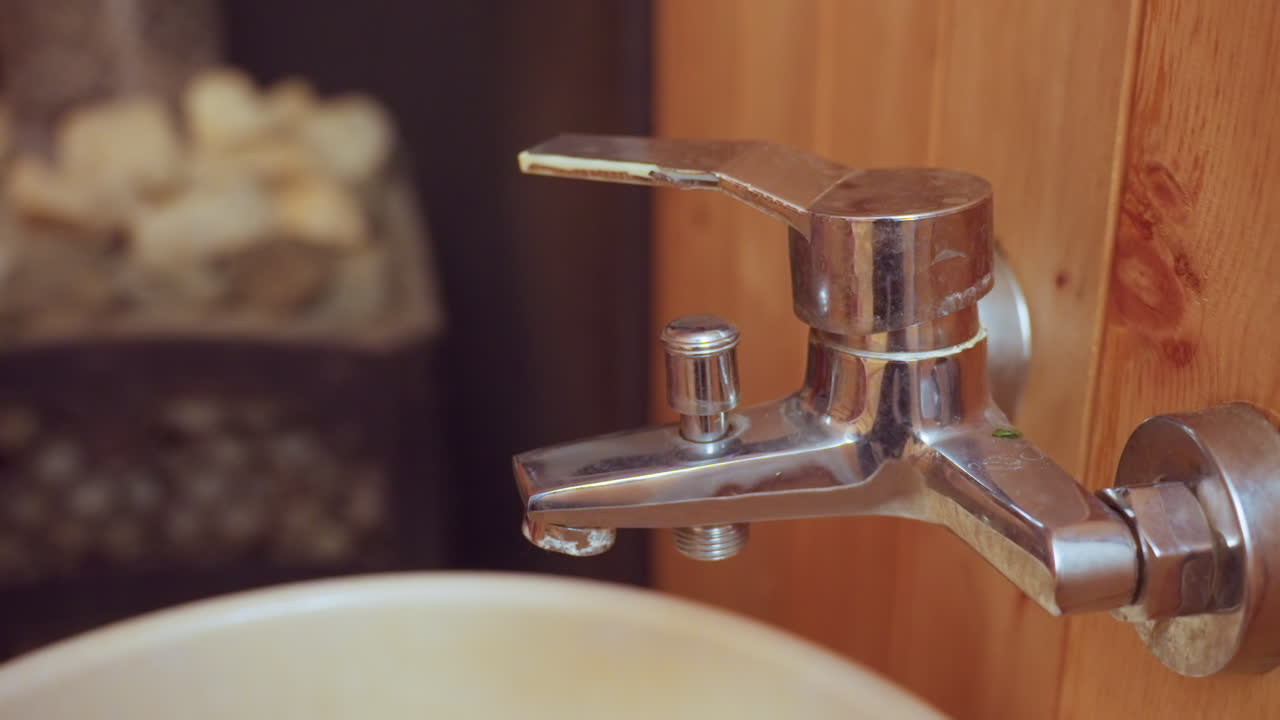 close up of person turning tap handle to release water into basin in wooden sauna bathroom, chrome faucet detail, hand with painted nails