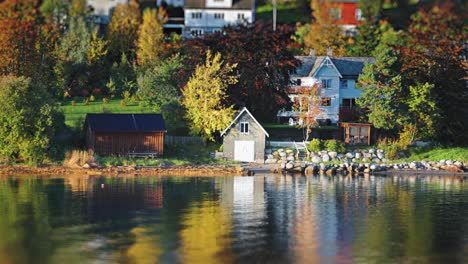 a cluster of homes overlooking a serene lake, set on a lush hillside with trees turning golden in autumn