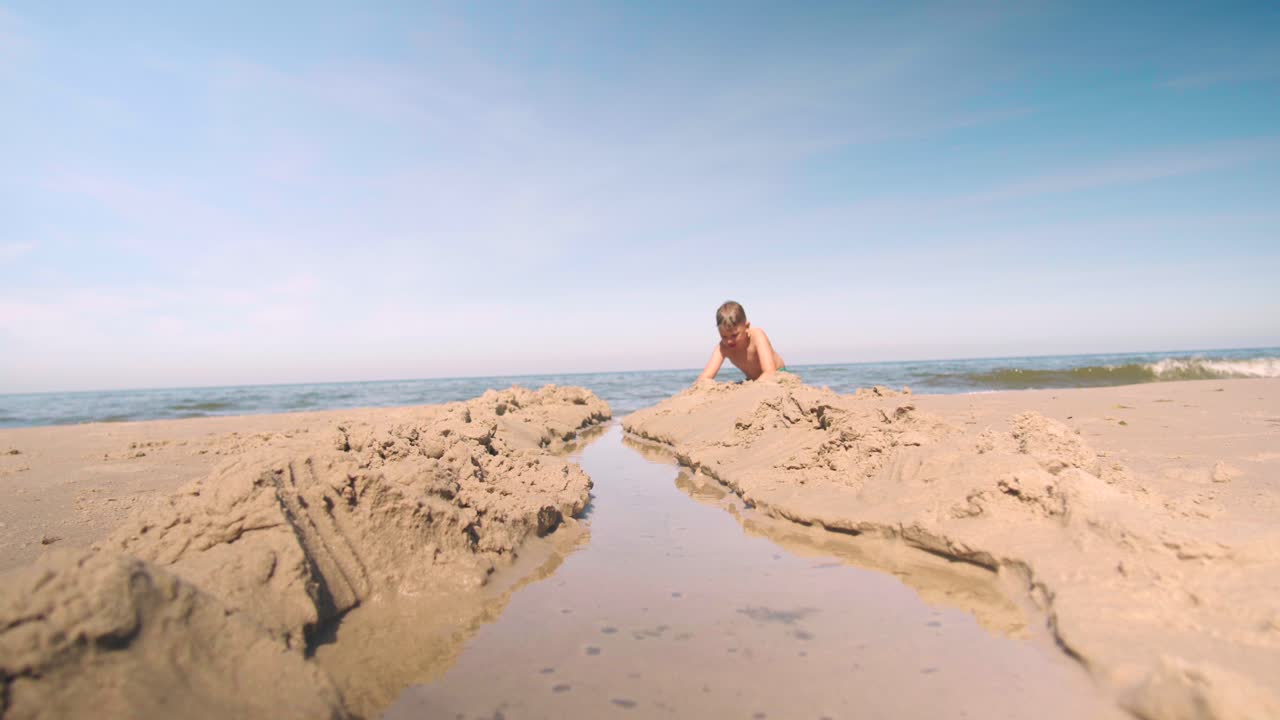 어린 소년이 해변에서 모래 속으로 길을 파고 있다