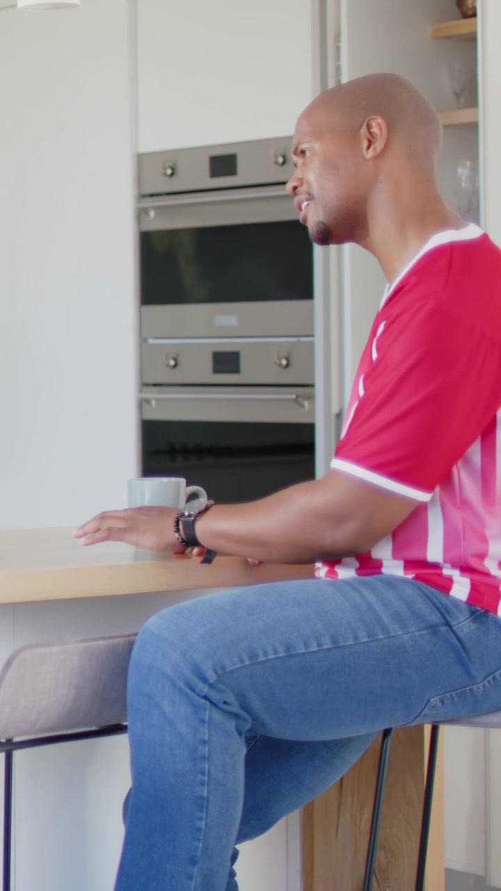 Man sitting at kitchen counter reaching for ceramic mug and gesturing while leading education demo