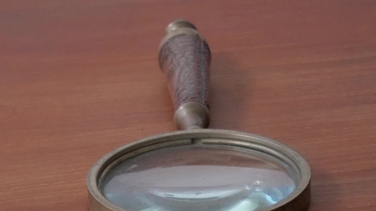 Detailed close-up of an antique magnifying glass with metal frame placed on wooden table