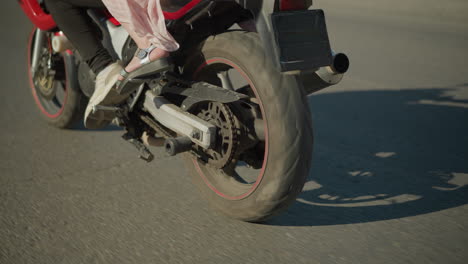 leg view of two ladies riding a power bike as the wind flutters their clothing, their shadows are cast on the road as the bike moves along