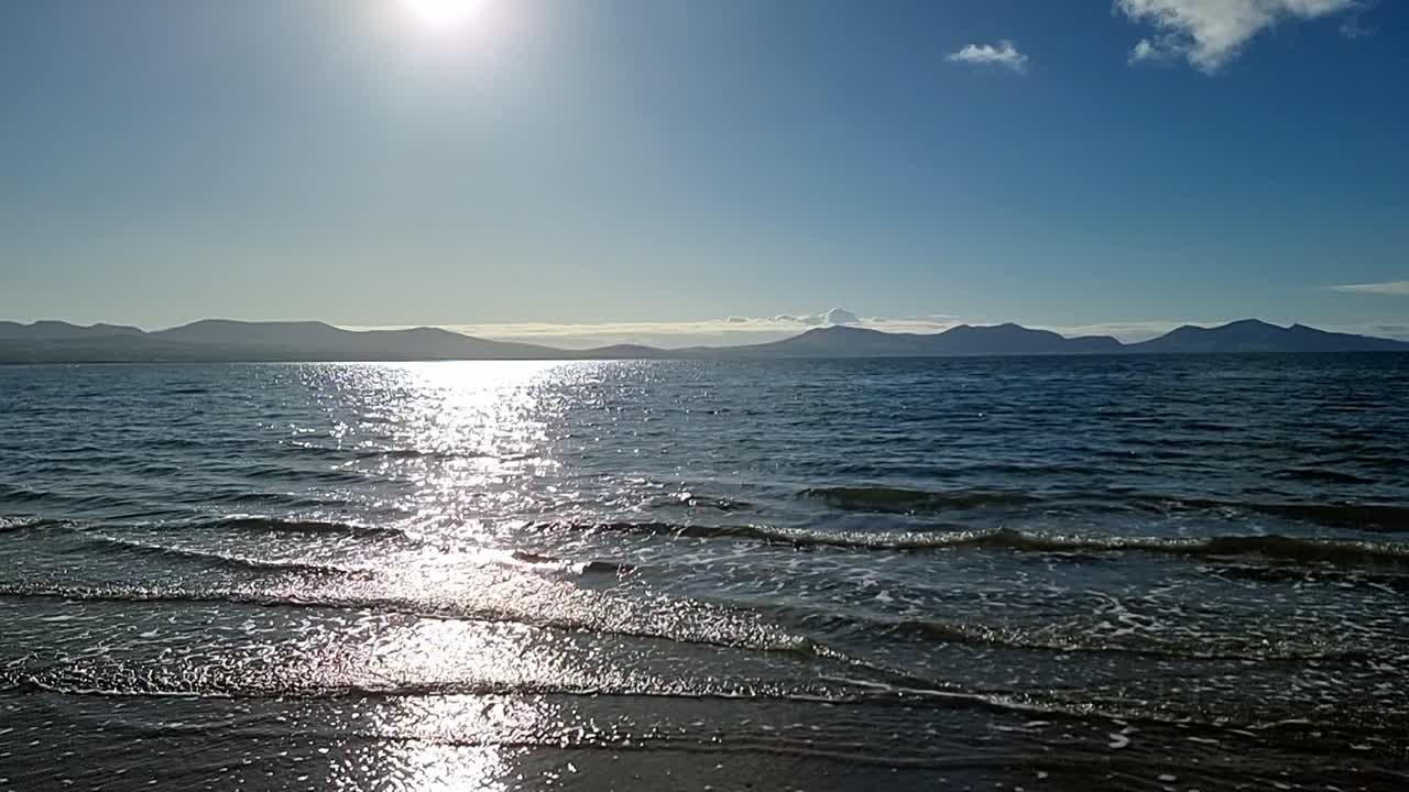 천천히 움직이는 반 ⁇ 이는 조류 파도가 하늘의 흐릿한 해가 뜨는 스노우도니아 산맥의 스카이라인 아래  ⁇ 어