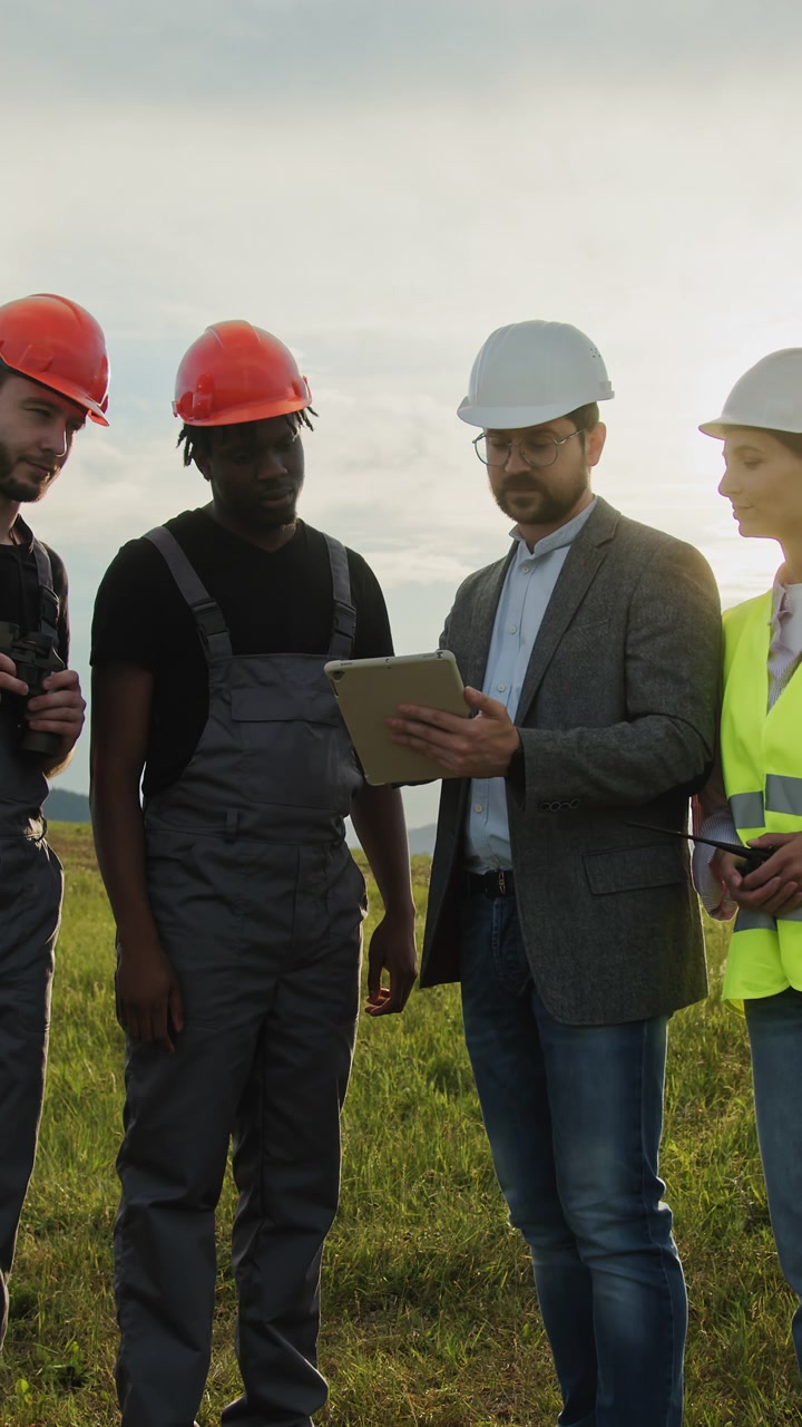 Diverse construction workers in hard hats and safety vests gather outdoors reviewing plans on a