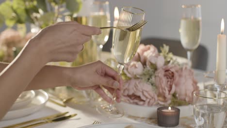 Close-Up-Of-Person-Tapping-Champagne-Glass-For-Quiet-Before-Speech-At-Table-Set-For-Meal-At-Wedding-Reception