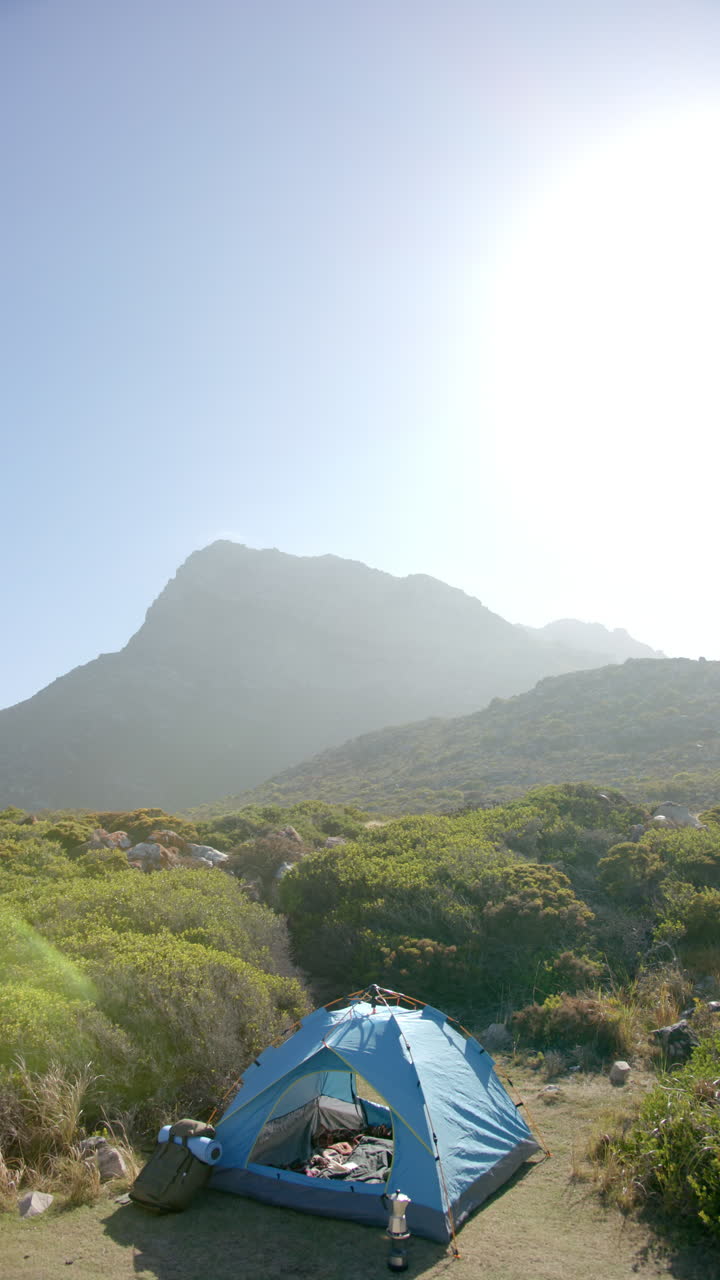 Vertical video: Camping in blue tent, hikers enjoying scenic mountain view in wilderness