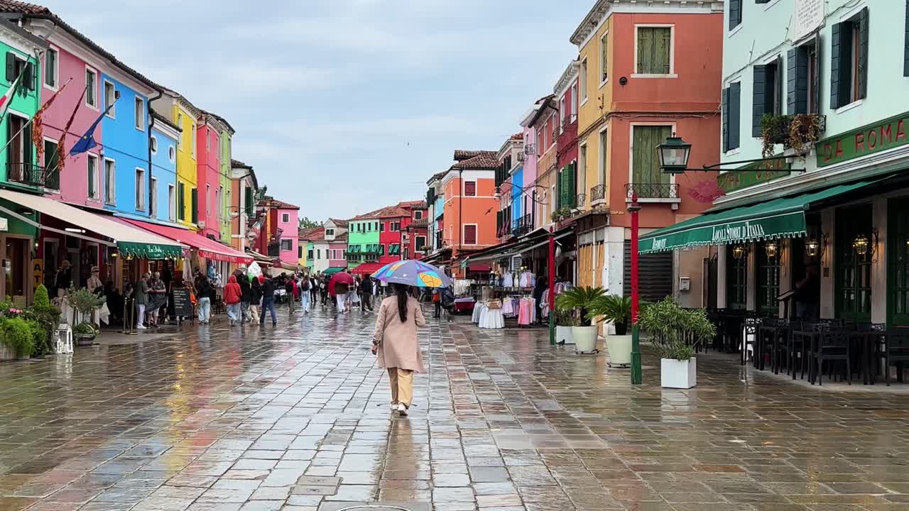 Colorful streets of Burano, Venice with people walking on a rainy day under umbrellas