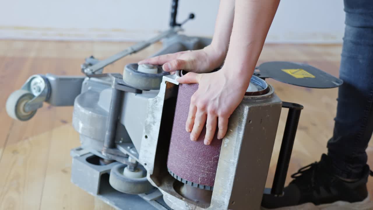 Worker replaces sanding belt on floor sander to prepare for wooden surface work
