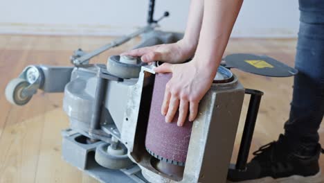 worker replaces sanding belt on floor sander to prepare for wooden surface work