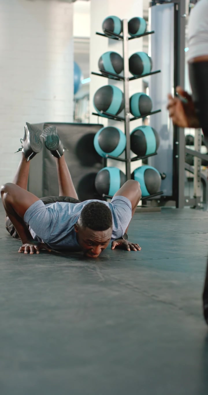 Video verticale: Uomo afroamericano che batte il cinque all'allenatore e si abbassa in posizione di plank per flessioni sul tappetino.