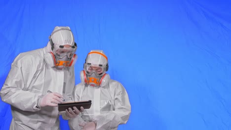 scientist virologist in respirator makes write in an tablet computer with stylus. man and woman wearing protective medical mask. chroma key blue.