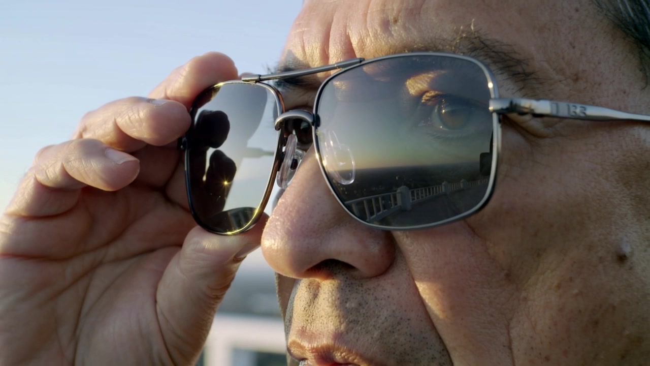 Adjusting senior male reacting to sun glare, holding aviator sunglasses on deck, peering at horizon