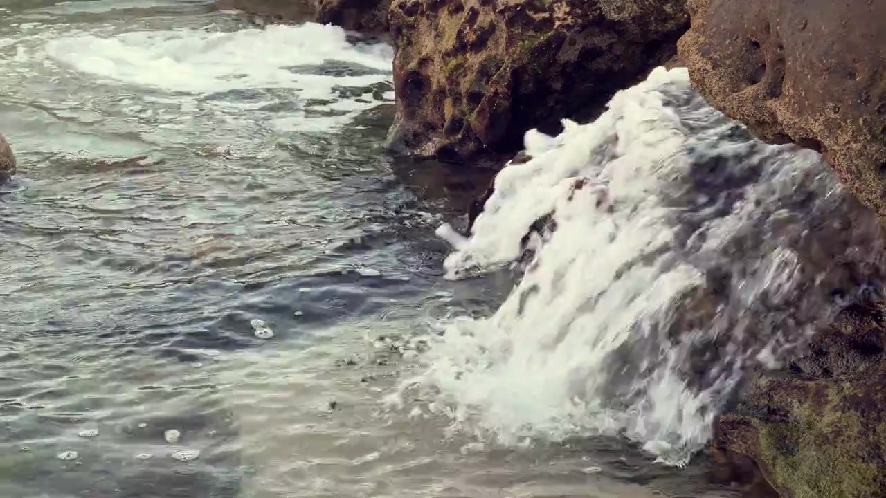 Acqua cristallina dell'oceano che scorre dolcemente sulle rocce a riva, creando una serena scena costiera.