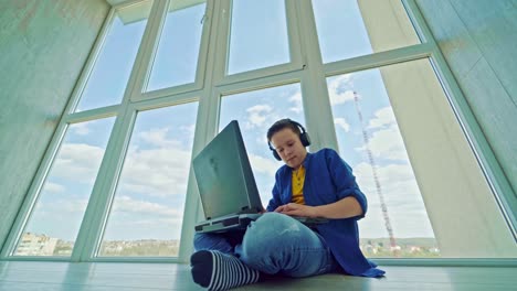 gaming at home. boy playing video games in his leisure time. teenager in earphones sitting near the window and playing on a laptop. happy boy wins the game.