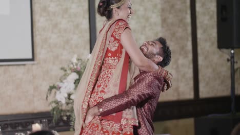 Cheerful-Newlywed-Couple-Dance-At-Wedding-Reception---Indian-Groom-Carrying-His-Bride-While-Turning-Around