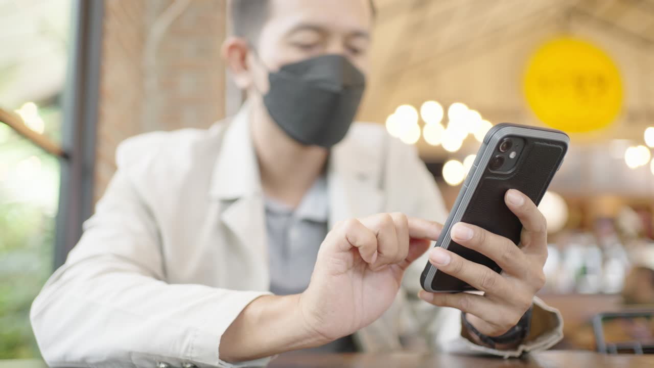 un joven empresario con una máscara quirúrgica está tomando una videoconferencia con los clientes a través de un teléfono inteligente conectado a internet.