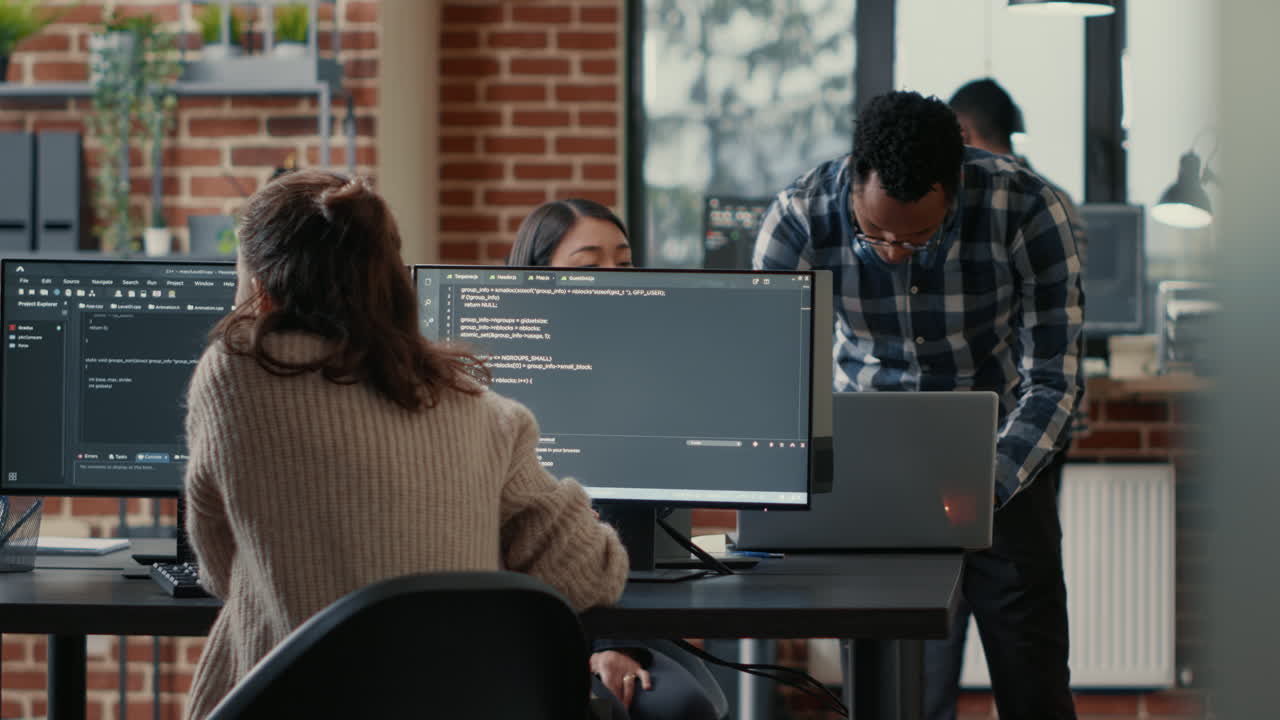Database programer writing code in front of multiple computer screens displaying artificial intelligence