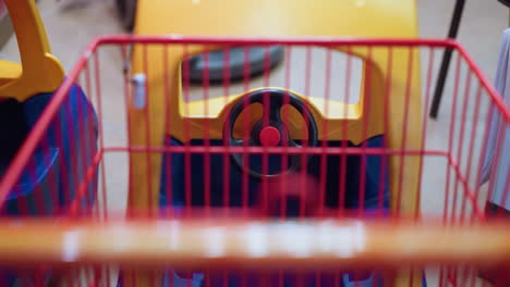 a close-up view of the interior of a children's shopping cart designed like a car, featuring a steering wheel and vibrant colors