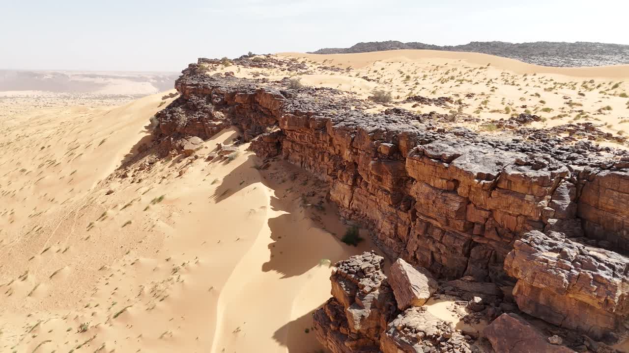 Drone aerial footage of Sahara desert in Mauritania. Golden sand dunes and dark rocky cliffs create a striking natural contrast in a vast arid wilderness