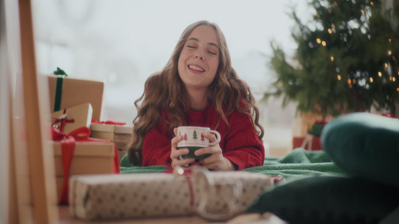 mujer feliz disfrutando de café fresco mientras yacía en el suelo durante la navidad
