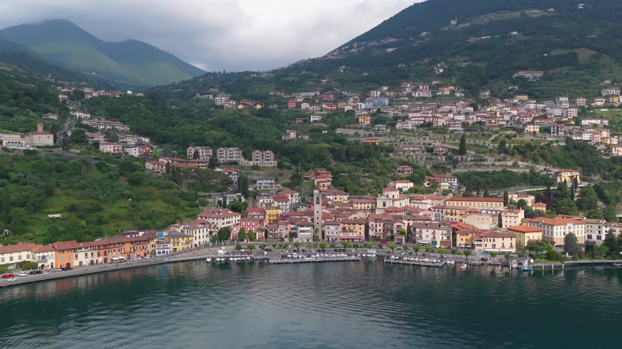 Wide drone shot of a picturesque Italian village nestled in green hills with vibrant facades lining the waterfront