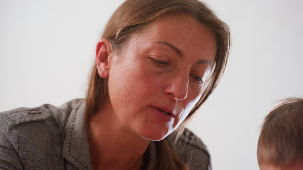 Instructor guiding kid during focused learning moment, close up of woman concentrated face with natural light, supportive presence highlighting teaching process