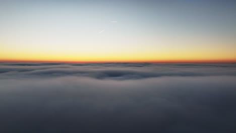 Dolly-aerial-shot-above-the-clouds-at-sunset-with-two-contrails-in-the-sky-and-a-beautiful-gradient-of-color-from-orange-to-blue