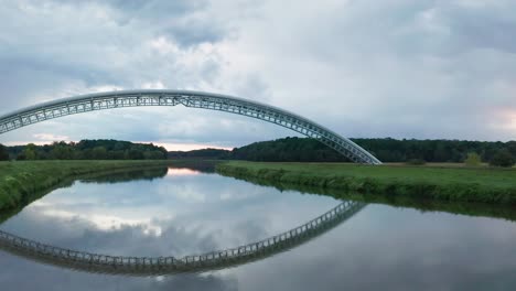 flying forward under gas pipes running across calm river moravia in slovakia. aerial sunset footage of two symmetrical gas pipe bridges reflecting in water