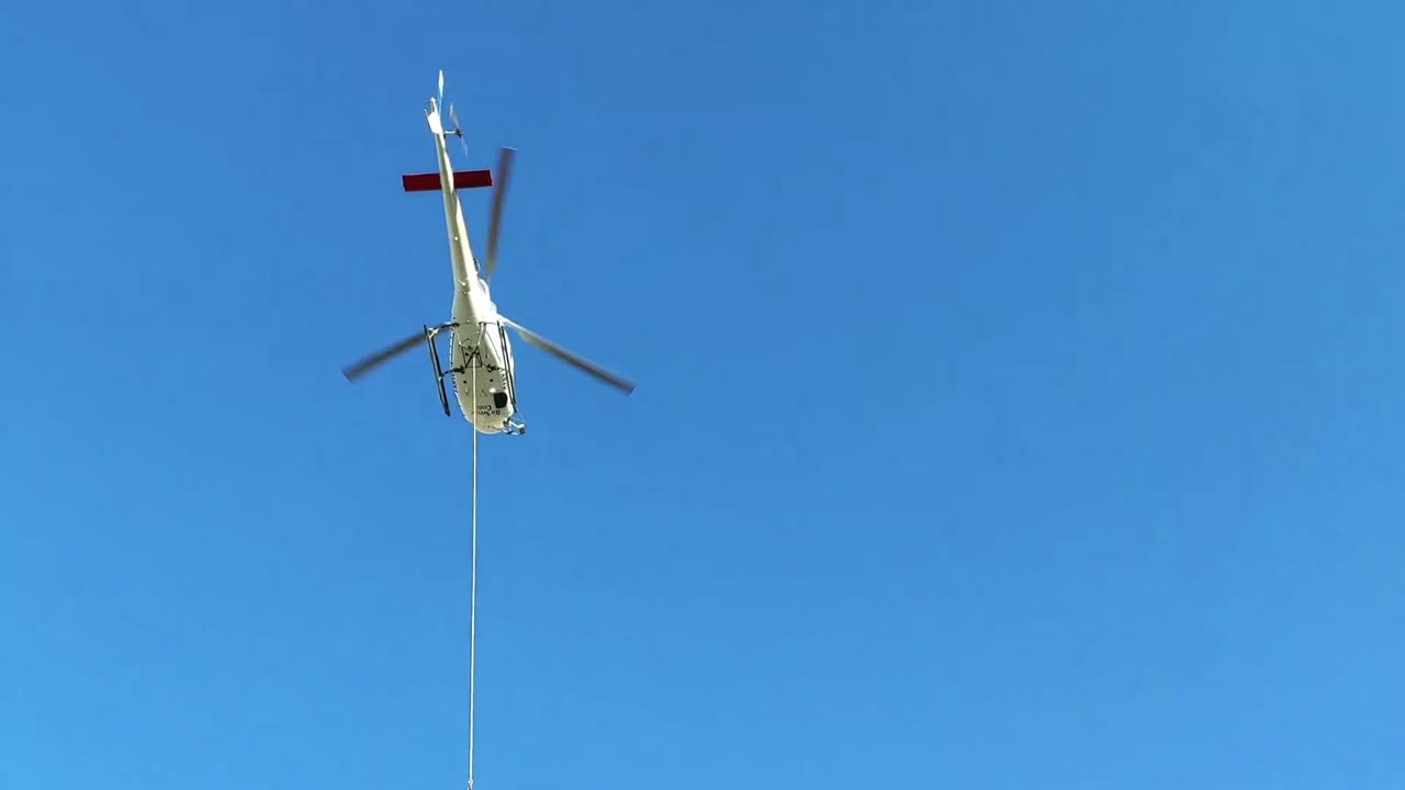 계곡 아래로 긴 강철 로프로 화물을 운반하는 높은 고산 목재 오두막 위의 헬리콥터