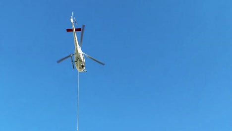 helicopter over high alpine wooden cabin transporting cargo on a long steel rope down the valley