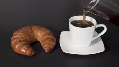 verter café de prensa francesa en una taza blanca junto a un croissant