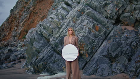 gorgeous model shooting beach at rocks closeup. smiling sexy girl holding mirror