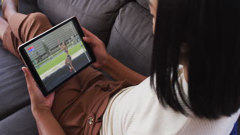 composite of woman sitting at home on couch watching athletics high jump event on tablet