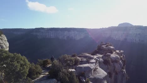 Aerial-view-of-man-walking-towards-cliff-edge-at-great-height,-tracking-shot