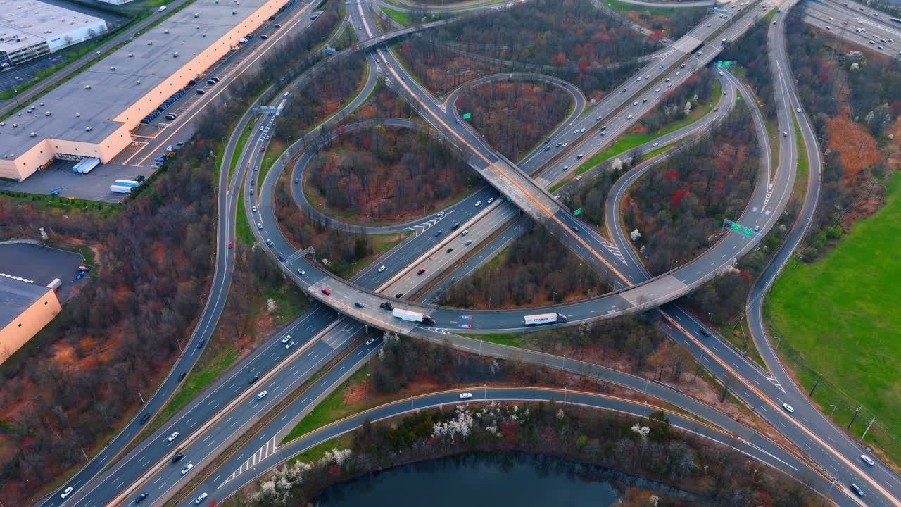 New York, USA, 5 October 2025: High angle view of logistics highway interchange with freight trucks. Aerial shot of semi trucks and cars driving through a complex multi lane road junction near warehouses