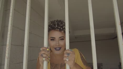 woman with short hair in a yellow dress smiling and dancing behind some bars in a parking lot